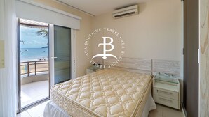 A bedroom with a large bed, a glass door leading to a balcony, a small bedside table, and an air conditioning unit on the wall. - Vista mar 2 suítes e piscina exterior (Florianópolis)
