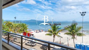 A beach view with a clear sky, palm trees, and boats in the water. - Vista mar 2 suítes e piscina exterior (Florianópolis)
