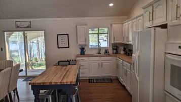 Une cuisine moderne avec des meubles blancs, une table à manger en bois et un four encastré.