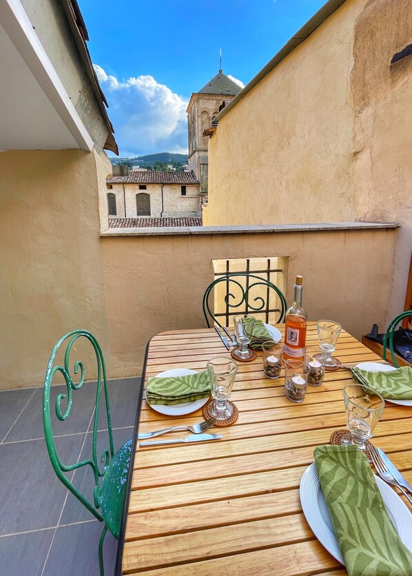 A wooden table set for two with a bottle of wine, glasses, and cutlery. A green chair is to the left.