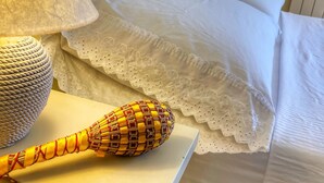 Siististi pedattu sänky, jossa on valkoiset lakanat ja pitsillä koristeltu tyyny. Punottu kori ja koriste-esine on asetettu yöpöydälle.