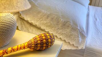 A neatly made bed with white linens and a lace-trimmed pillow. A woven basket and a decorative item are placed on the bedside table.