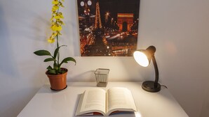 A white desk with an open book, a potted plant, a framed picture of the Eiffel Tower, and a desk lamp. - Apartamento 2 Quartos - Praça Pôr do Sol (São Paulo)