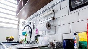 A kitchen with white tiles, a hanging rack with utensils, a sink, and a window. - Apartamento 2 Quartos - Praça Pôr do Sol (São Paulo)