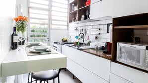A modern kitchen with white cabinets, a built-in microwave, and a window with blinds. - Apartamento 2 Quartos - Praça Pôr do Sol (São Paulo)