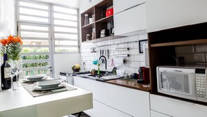 A modern kitchen with white cabinets, a microwave, and a window with blinds. - Apartamento 2 Quartos - Praça Pôr do Sol (São Paulo)