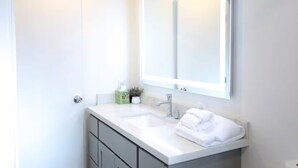 Ein modernes Badezimmer mit einem weißen Waschtisch, einem großen Spiegel und einem Handtuchhalter.