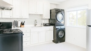 A modern kitchen with white cabinetry, a black stove, a sink, and a stacked washer and dryer. - Comfy 2BR Apt w/ AC/Washer/Dryer/EV - in Sunnyvale (Sunnyvale)