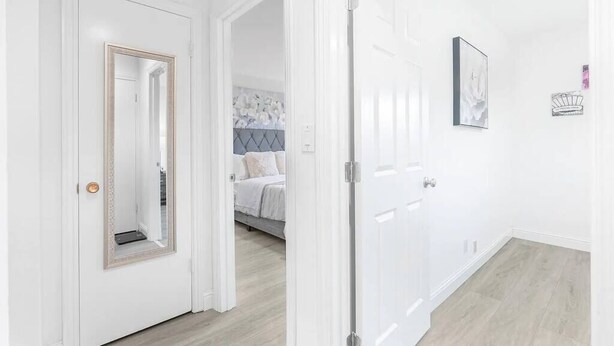 A hallway with white walls and a wooden floor, leading to a bedroom with a bed and a headboard. - Comfy 2BR Apt w/ AC/Washer/Dryer/EV - in Sunnyvale (Sunnyvale)