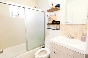 A bathroom with a bathtub, toilet, and a vanity with a mirror and shelves.