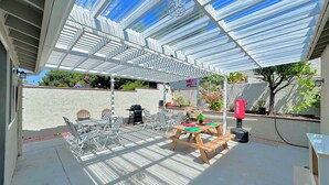 Une terrasse extérieure dotée d’un espace salon couvert, d’un barbecue et de plantes en pot.
