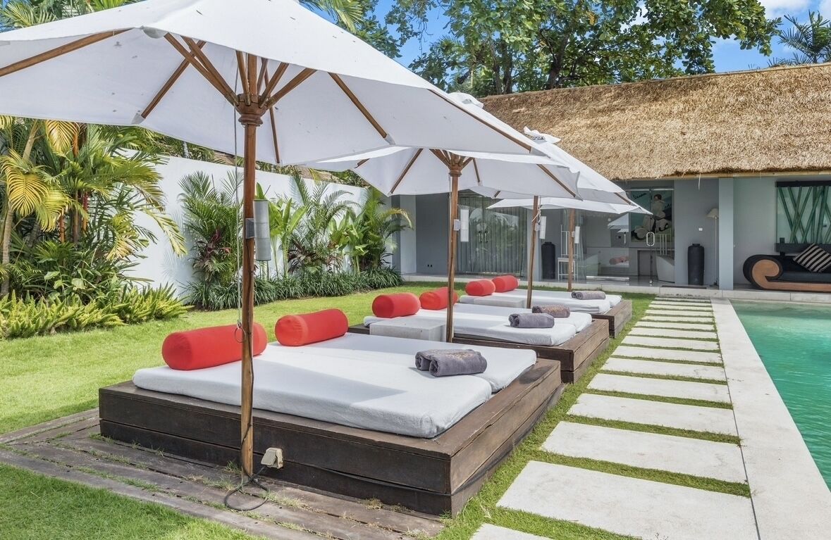 A poolside area with sunbeds and umbrellas, surrounded by lush greenery.