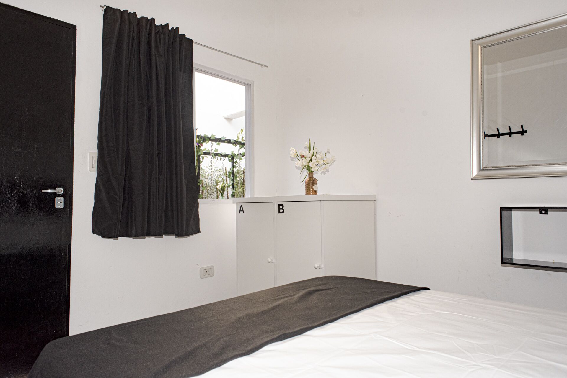 A bedroom with a bed, a window with curtains, a bedside table with a vase of flowers, and a wardrobe with two doors labeled A and B.