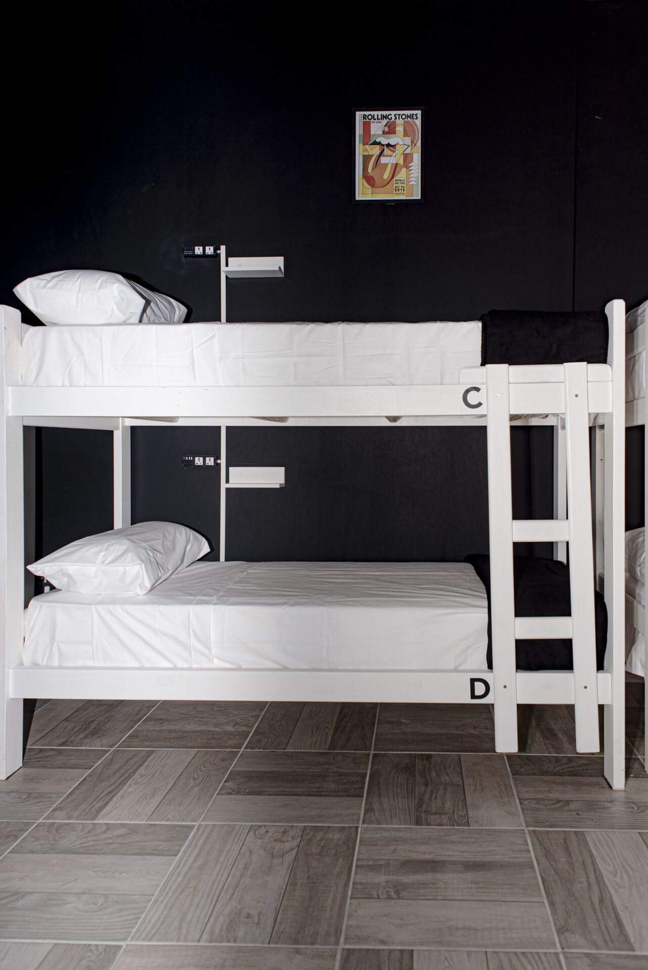 A bunk bed with two levels, labeled C and D, in a room with dark walls and a poster on the wall.