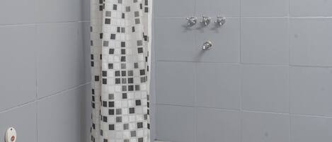 A shower area with a white shower curtain featuring a black square pattern, grey tiled walls, and a showerhead.