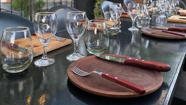 A dining table set outdoors with multiple wine glasses, wooden coasters, and cutlery. - PH Palermo Hostel (Buenos Aires)