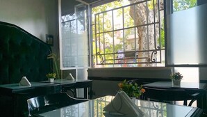 A room with a glass table, two chairs, a green upholstered headboard, and a window with metal bars. - PH Palermo Hostel (Buenos Aires)