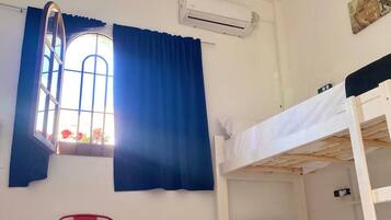 Una habitación pequeña con una litera, una silla roja, una mesita y una ventana con cortinas.