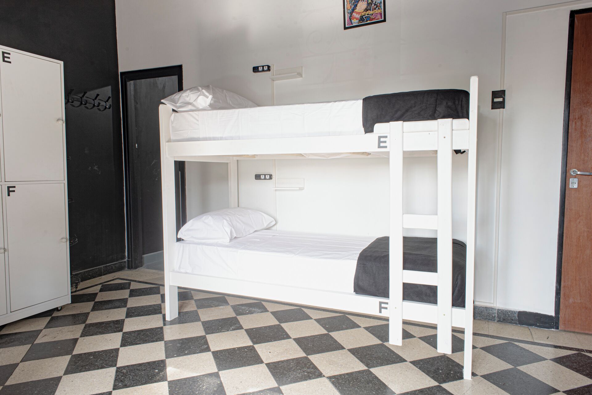 A bunk bed in a room with a checkered floor, a wardrobe, and a door.