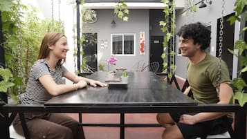 A dining area with a table and chairs, surrounded by hanging plants and a view of the interior.