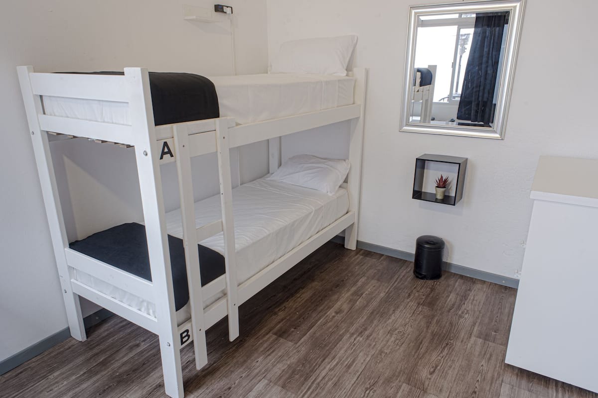 Habitación con literas, un escritorio pequeño, un espejo y una planta en maceta.