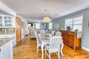 A spacious kitchen with a dining table, white chairs, and a wooden cabinet.