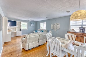 A spacious living area with a sofa, dining table, and chairs, a kitchen area with a coffee machine, and a ceiling fan.