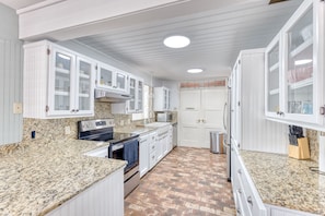 A kitchen with white cabinets, granite countertops, a stove, and a microwave.