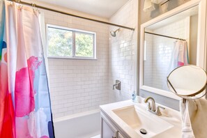 A bathroom with a bathtub, a shower, a sink, and a window.