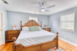 A bedroom with a wooden bed, two nightstands, a ceiling fan, and a window with blinds.