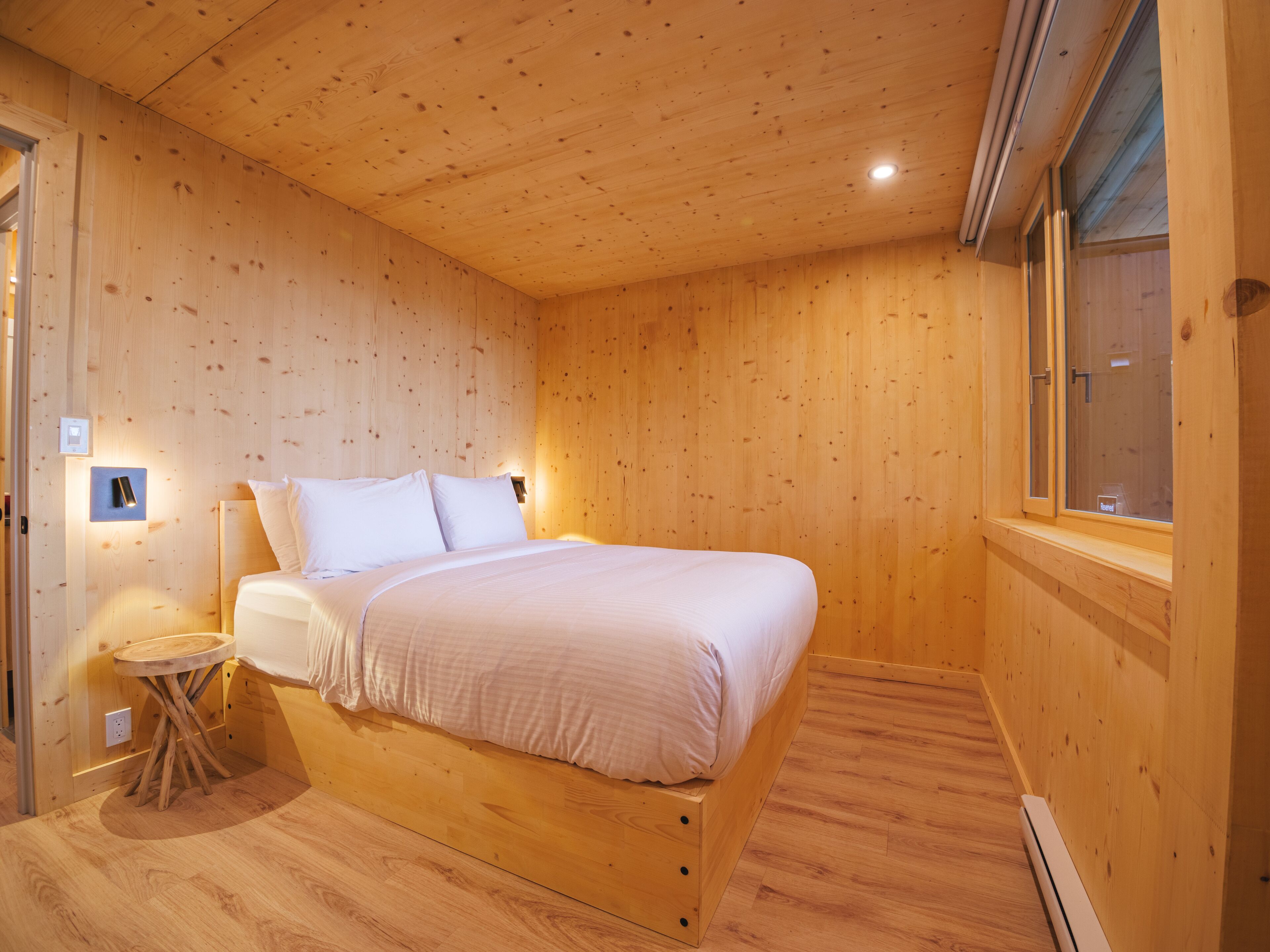 Camera da letto con pannelli in legno, un letto, un comodino e una finestra.