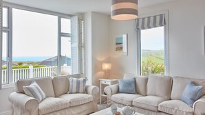 A living room with two beige sofas, a small side table with a lamp, and a view of the outdoors through large windows.