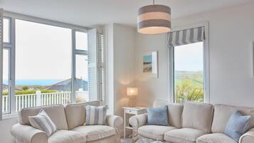 A living room with two beige sofas, a small side table with a lamp, and a view of the outdoors through large windows.