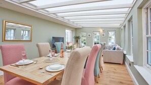 A dining area with a wooden table set for four, surrounded by chairs with a checkered pattern. A large mirror hangs on the wall, and there is a sofa in the background.