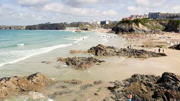 A coastal beach with rocky areas, a sandy shore, and buildings in the background.
