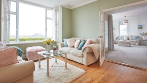 A spacious living room with a large window, a white sofa, a glass coffee table, and a view of the outdoors.