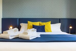 A neatly made bed with white linens, a blue bedspread, and two pillows in yellow and blue.