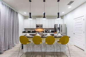 A modern kitchen with white cabinets, a stainless steel refrigerator, and a dining area with yellow chairs.