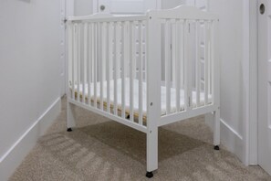 A white crib in a hallway with carpeted flooring and white walls.