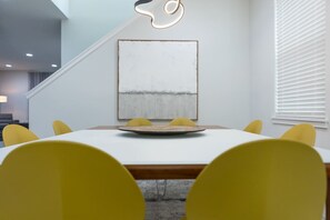 Un comedor moderno con una mesa blanca, sillas amarillas y un cuadro abstracto grande en la pared.