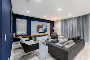 A modern living room with a grey sofa, a black armchair, a coffee table, and a TV mounted on the wall.