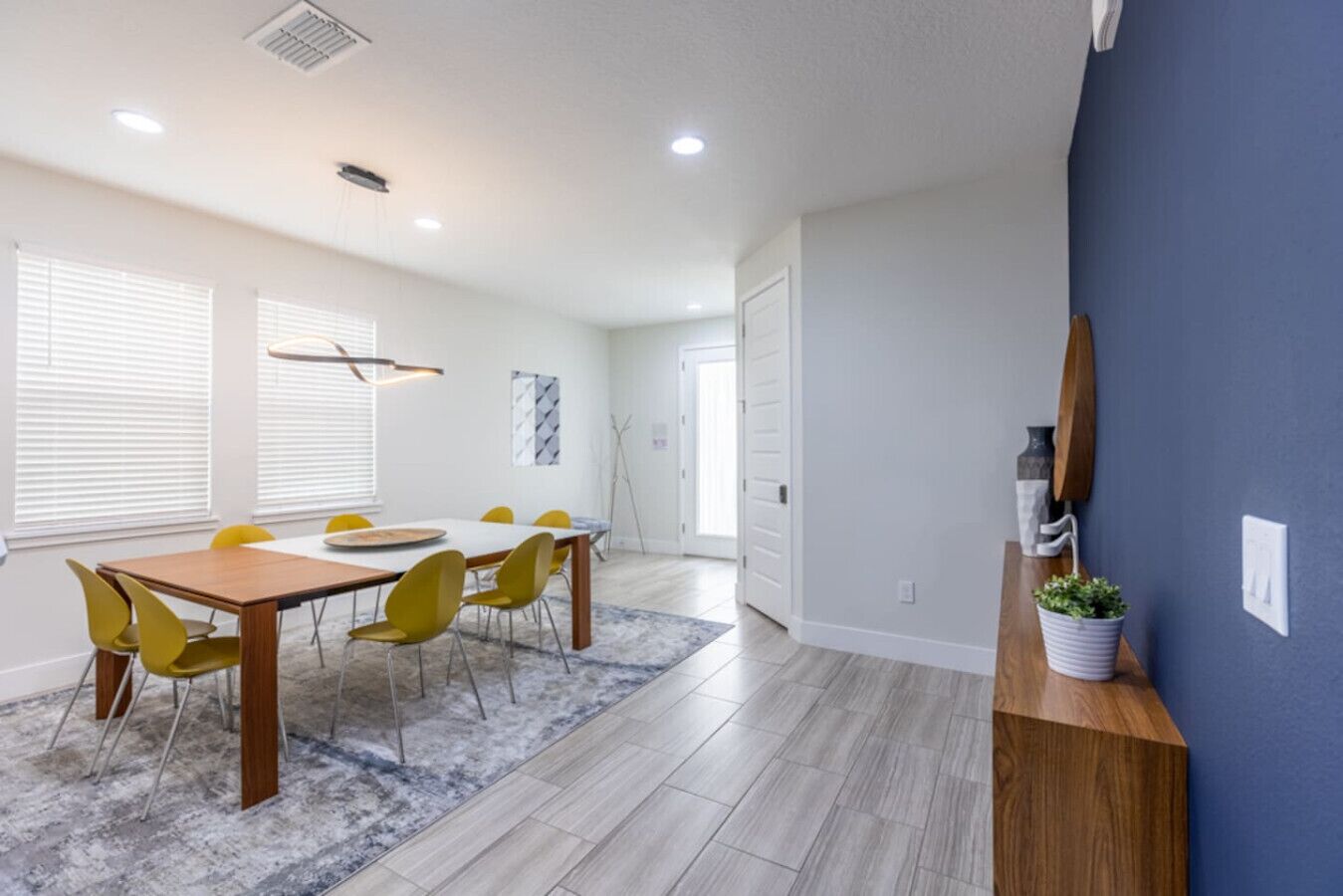 Une pièce spacieuse avec une table à manger en bois et des chaises jaunes, un mur d’accent bleu et un luminaire moderne.