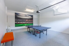A room with a ping pong table, a projector, and a large mural of a stadium.