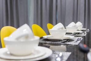A dining table set with white bowls and plates, yellow chairs, and a reflective surface.