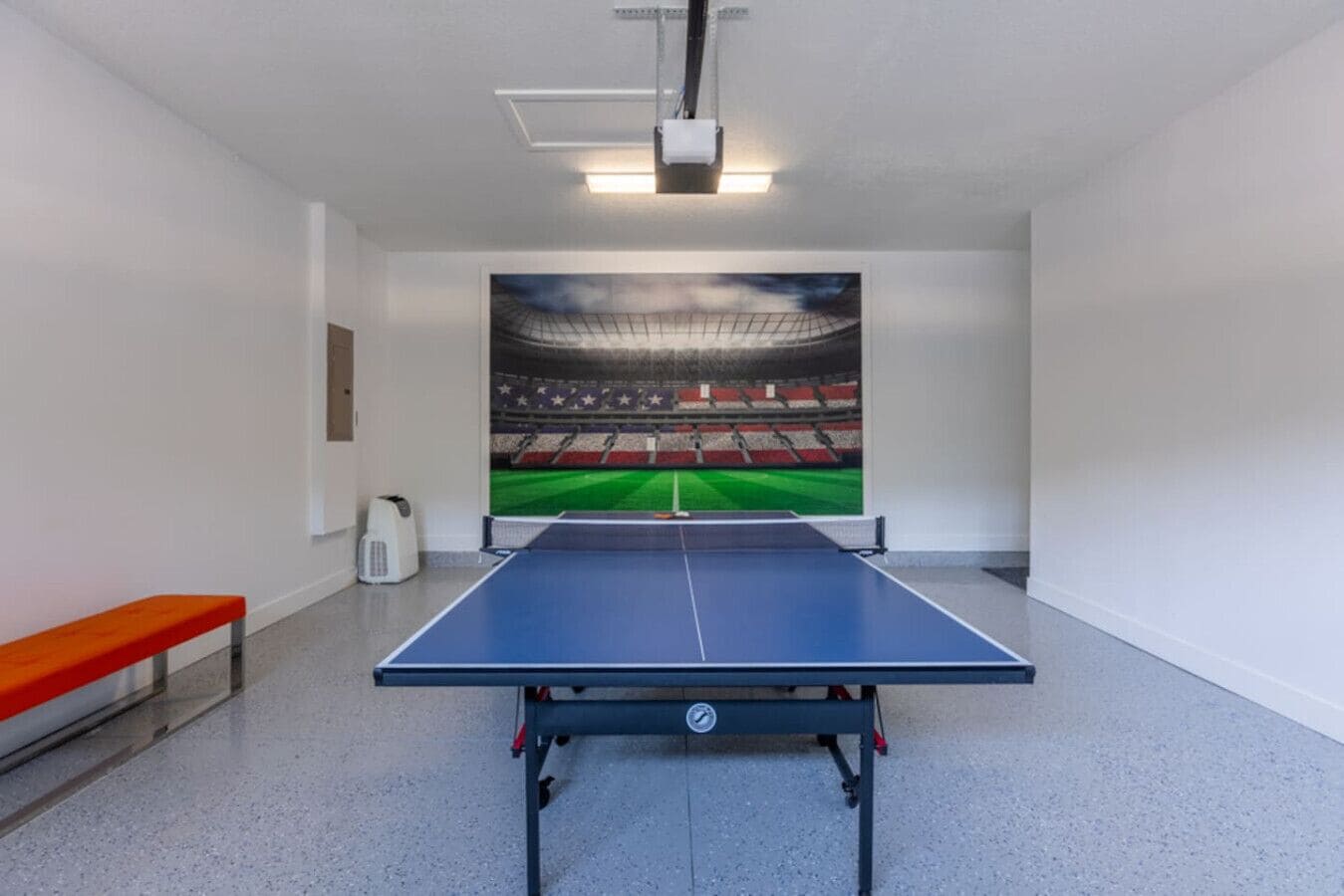 Une table de ping-pong se trouve dans une pièce dont un des murs est orné d’une grande fresque représentant un stade.