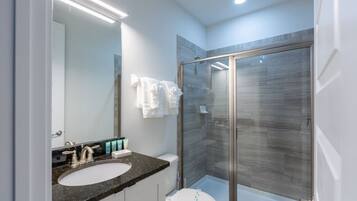 A modern bathroom with a glass-enclosed shower, a sink with a marble countertop, and a toilet.