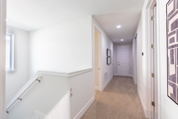 A narrow hallway with white walls, a beige carpet, and a white door at the end.