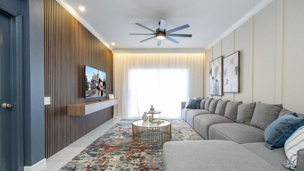 Un salon moderne avec un canapé, une table basse, un téléviseur fixé sur un mur recouvert de panneaux en bois et un ventilateur de plafond.