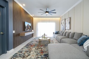 Una sala de estar moderna con un sofá, una mesa de centro, un televisor montado en una pared de paneles de madera y un ventilador de techo.