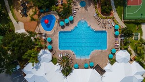 Vue aérienne d’un espace piscine comprenant une grande piscine, des piscines plus petites et des zones de détente avec des parasols.